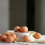 Still life of organic brown eggs in a ceramic bowl on a neutral cloth, showcasing natural textures and a rustic feel.
